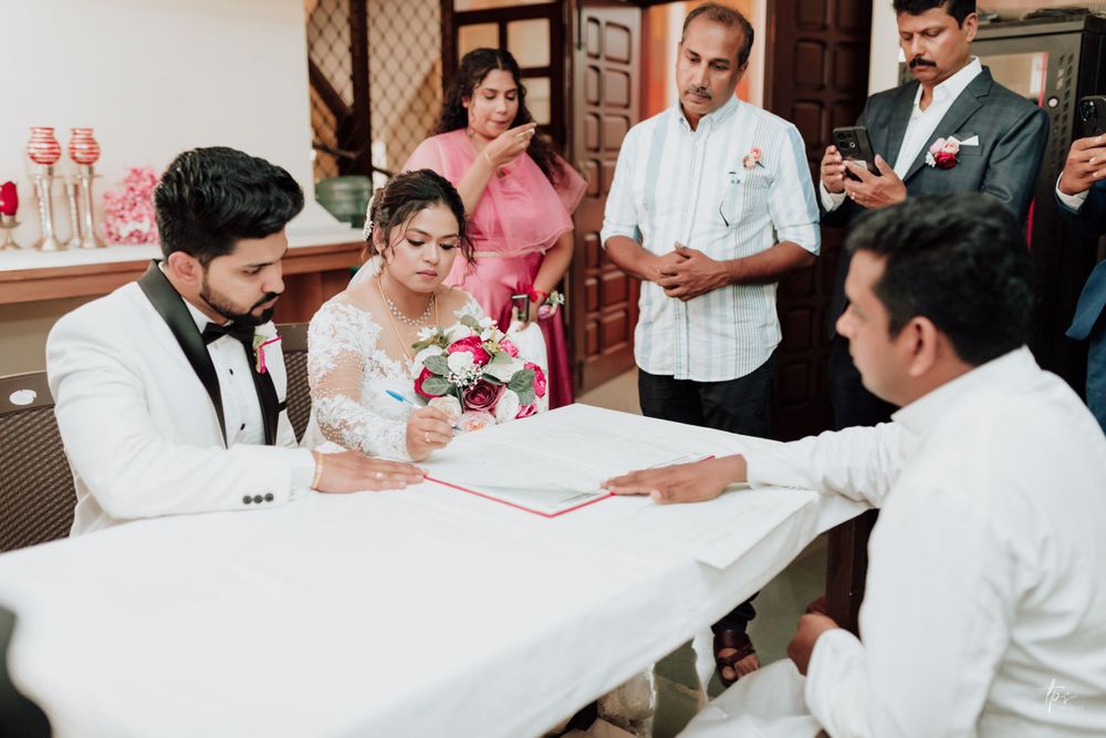 Wedding guests gather around tables to sign ceremonial documents.