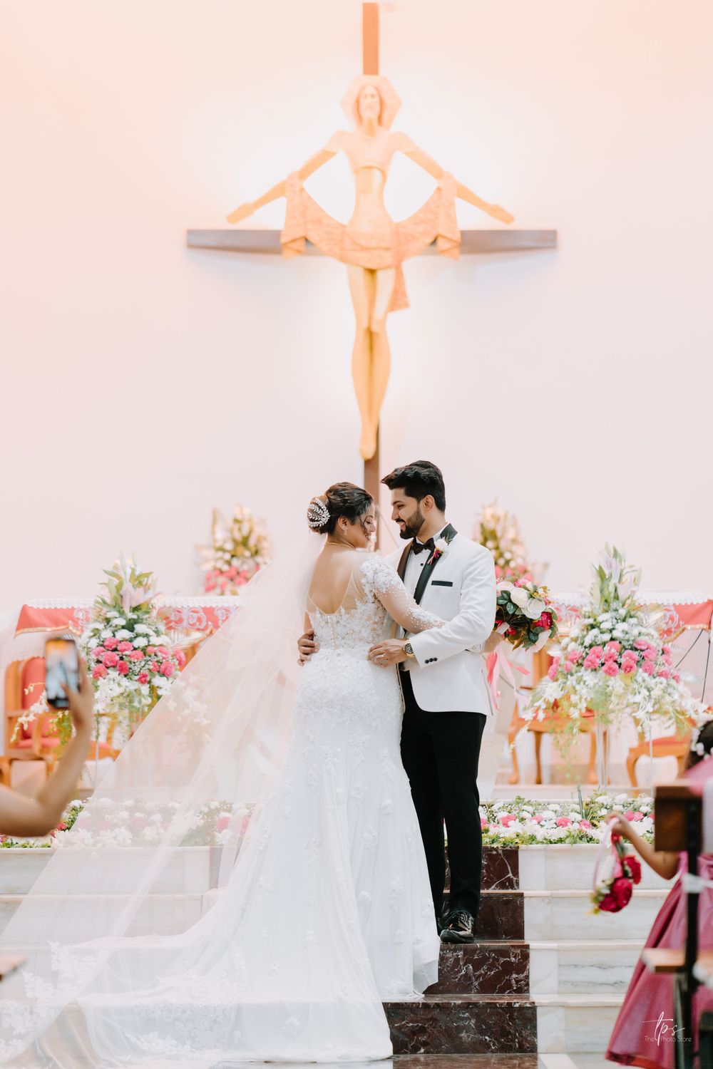Newlyweds share romantic moment in front of church altar with pink floral decorations.