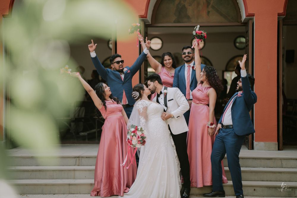 Wedding party celebrates joyfully under coral-colored arched architecture.