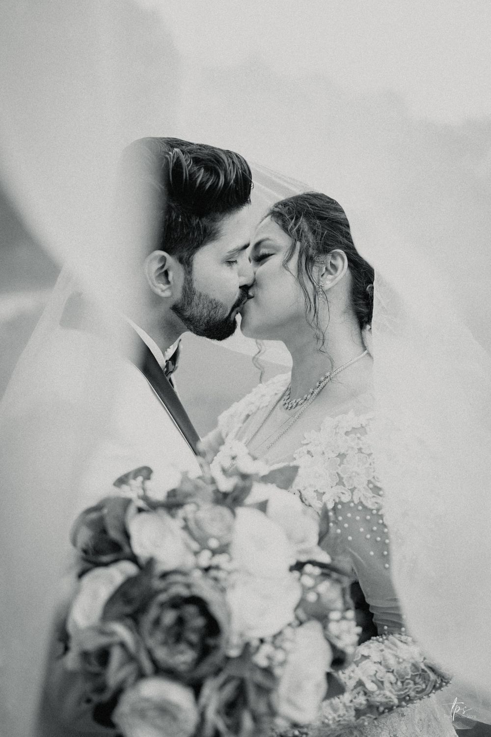 Romantic black and white wedding photo showing tender embrace with pink and white floral bouquet.