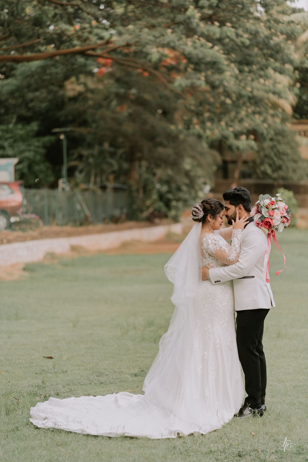 Wedding couple dancing playfully on grassy lawn surrounded by trees.