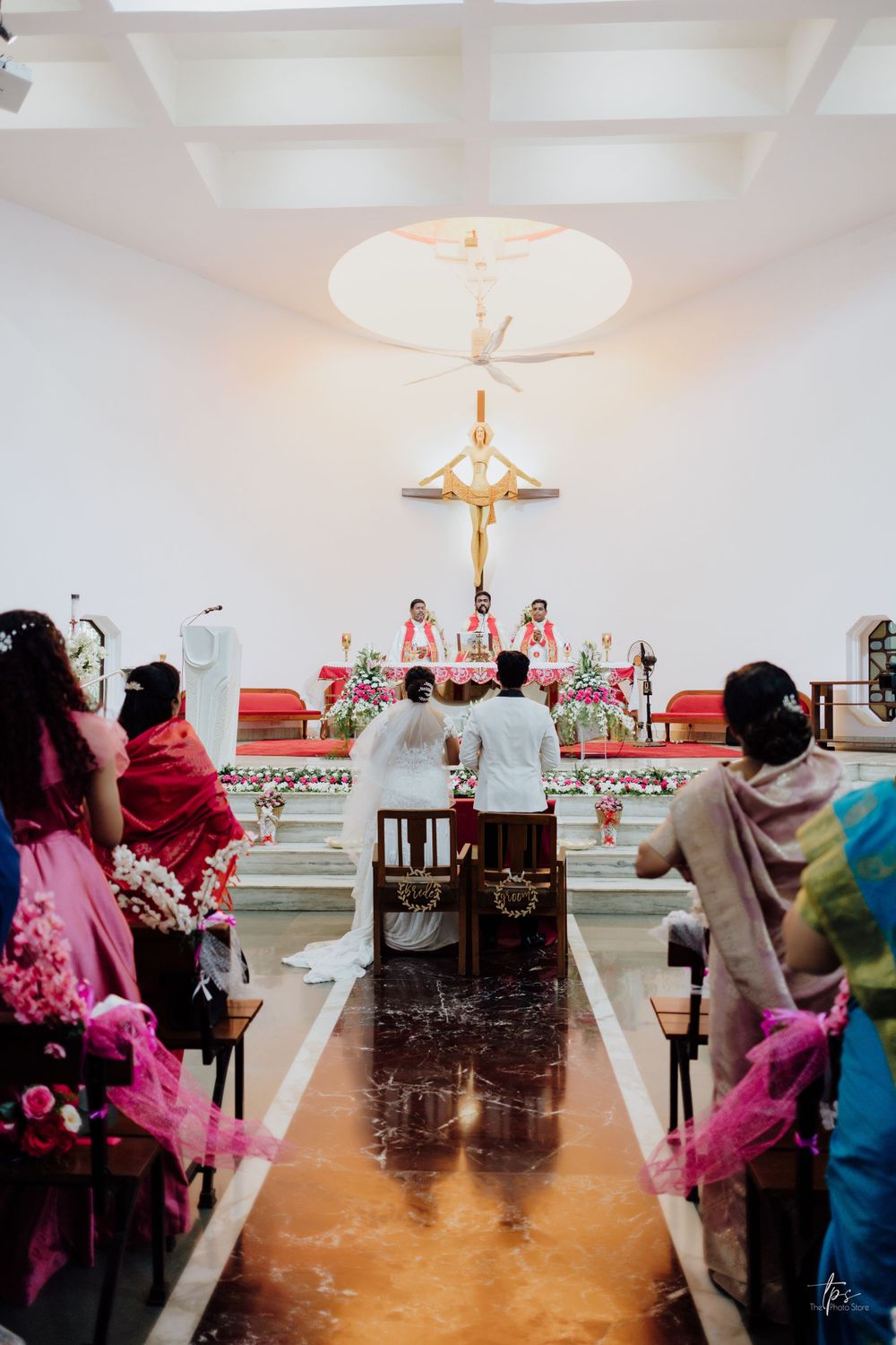 Wedding ceremony in progress with pink decorations and white vaulted ceiling.