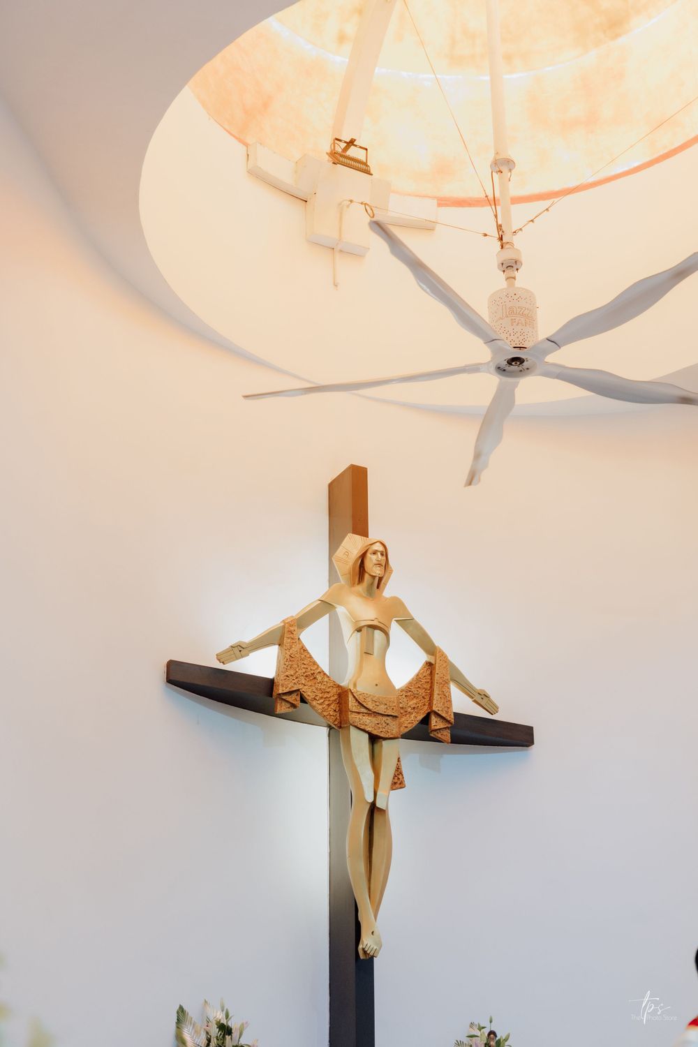 Decorative wooden crucifix mounted on light colored wall with soft lighting.
