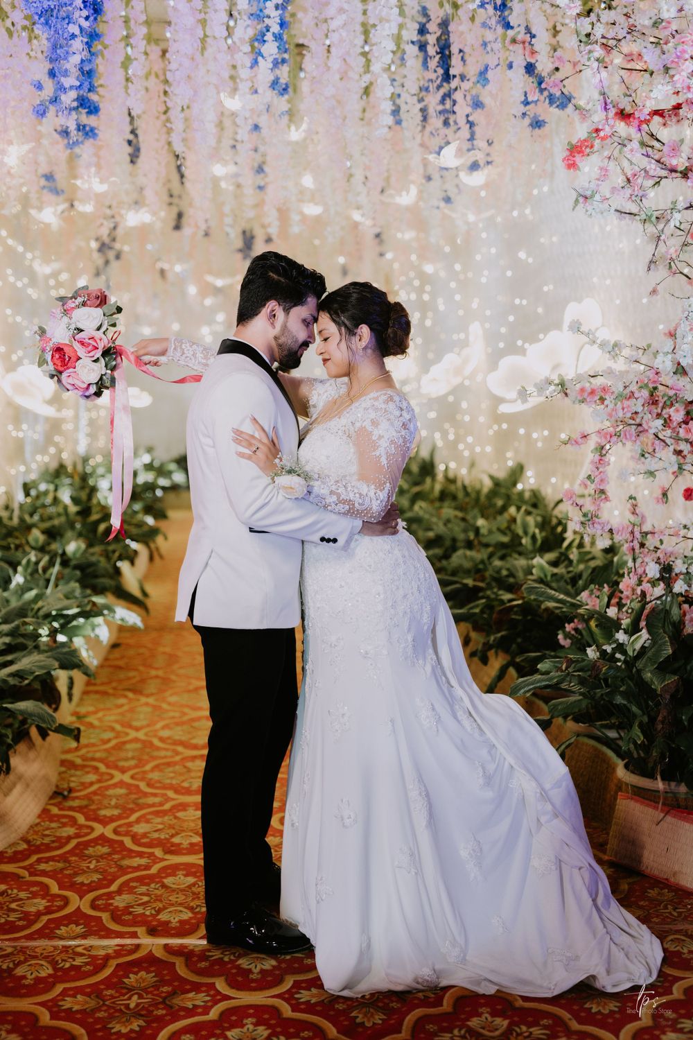 A romantic wedding moment captured under cascading floral decorations and twinkling lights.