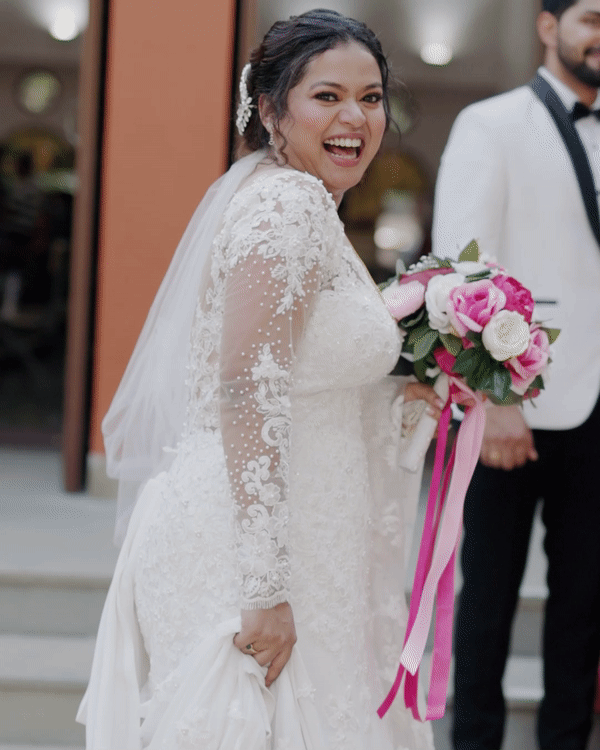 Bride in white lace gown holds pink bouquet during wedding celebration.