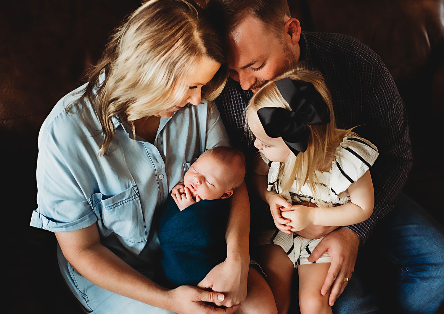 An intimate family moment as they gather close together to look at their sleeping newborn baby.