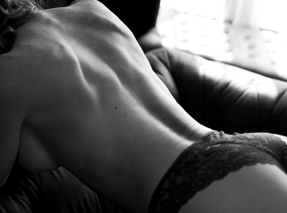 A woman in black lingerie poses topless kneeling on couch for the best boudoir photographer in the Phoenix Arizona area