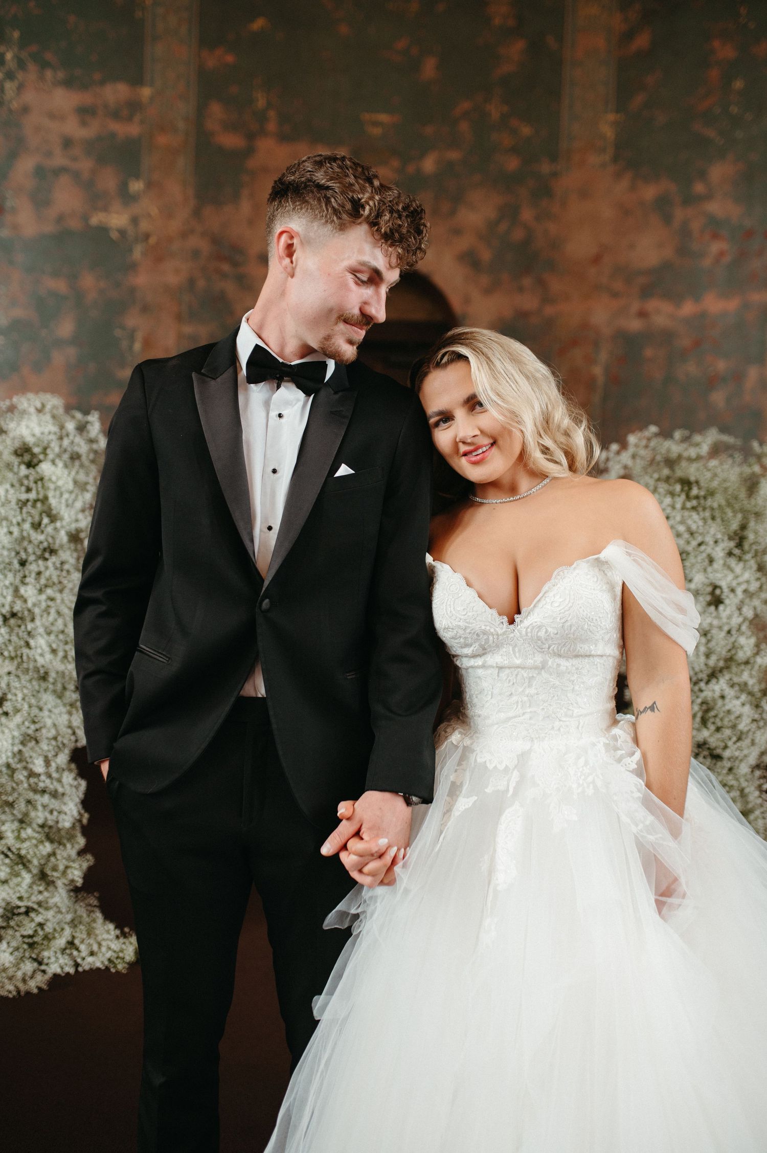 A formal wedding portrait of a couple in elegant attire against a textured backdrop.