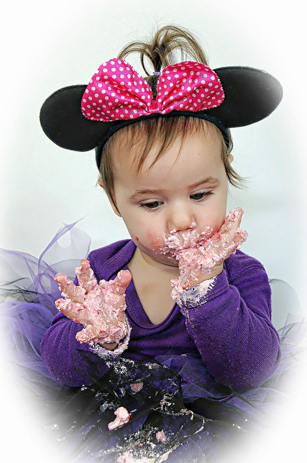Baby in purple dress wearing Minnie Mouse ears and sparkly gloves.