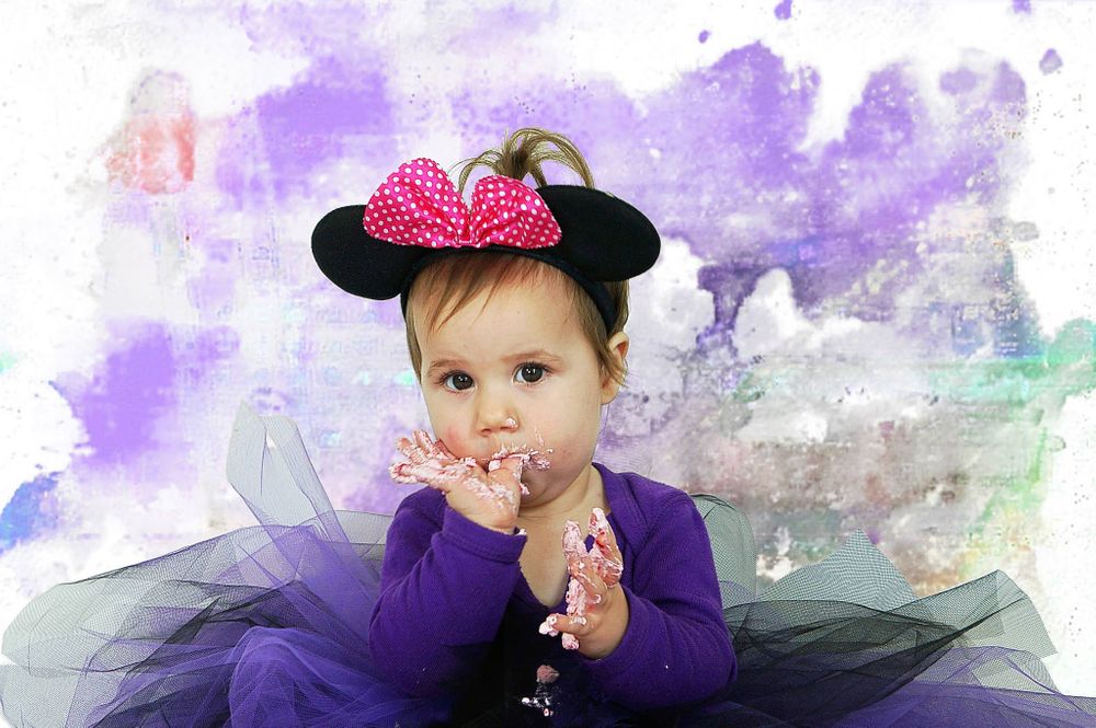 Baby in purple tutu and Minnie Mouse ears against watercolor background.
