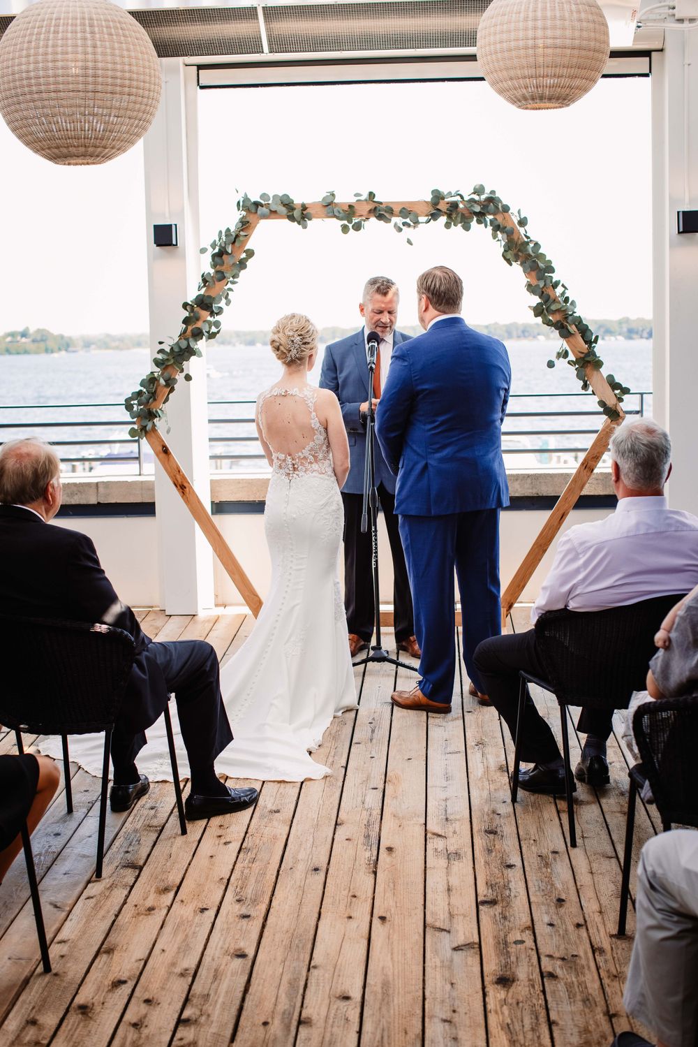 Wedding ceremony under a floral arch with paper lanterns and waterfront backdrop.