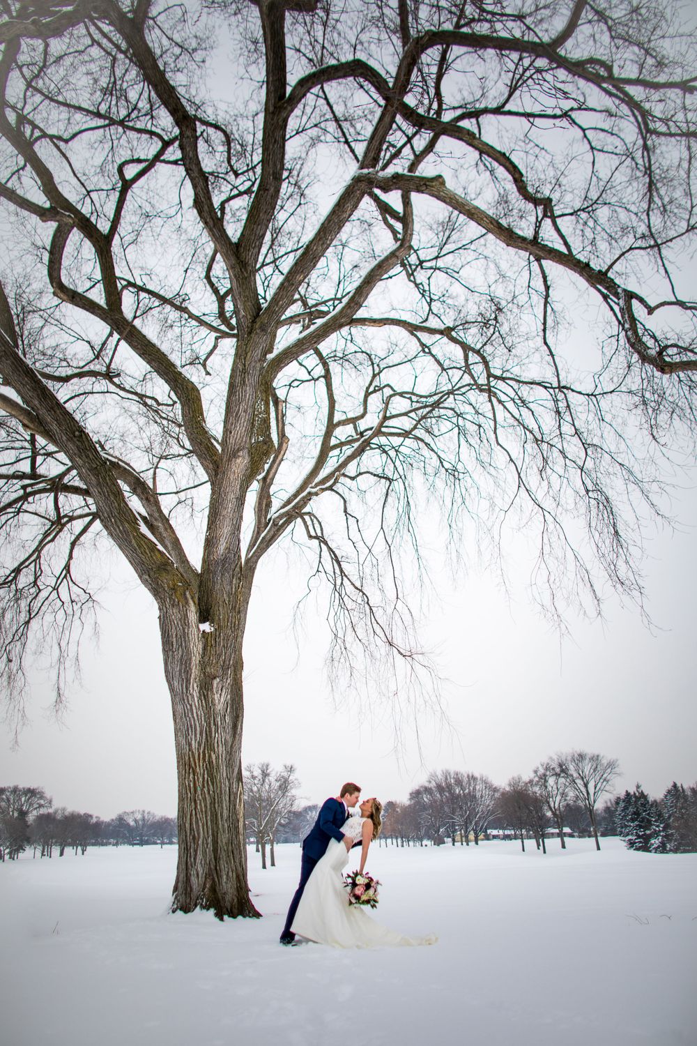 A couple shares a romantic moment under a snow-covered tree in a winter landscape.