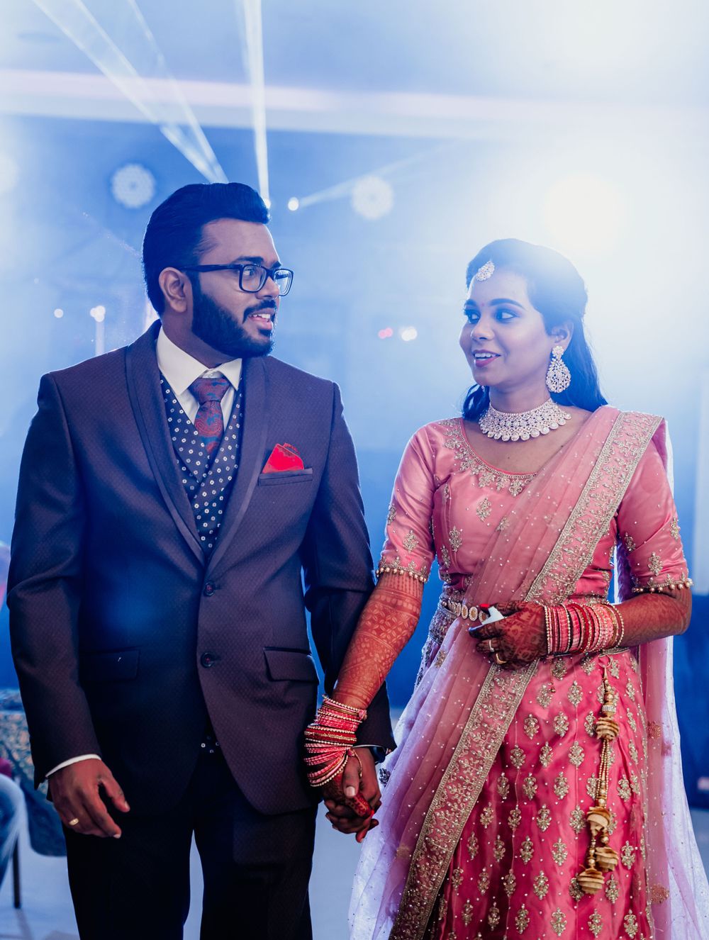 A couple dressed in formal wedding attire hold hands while exchanging loving glances.