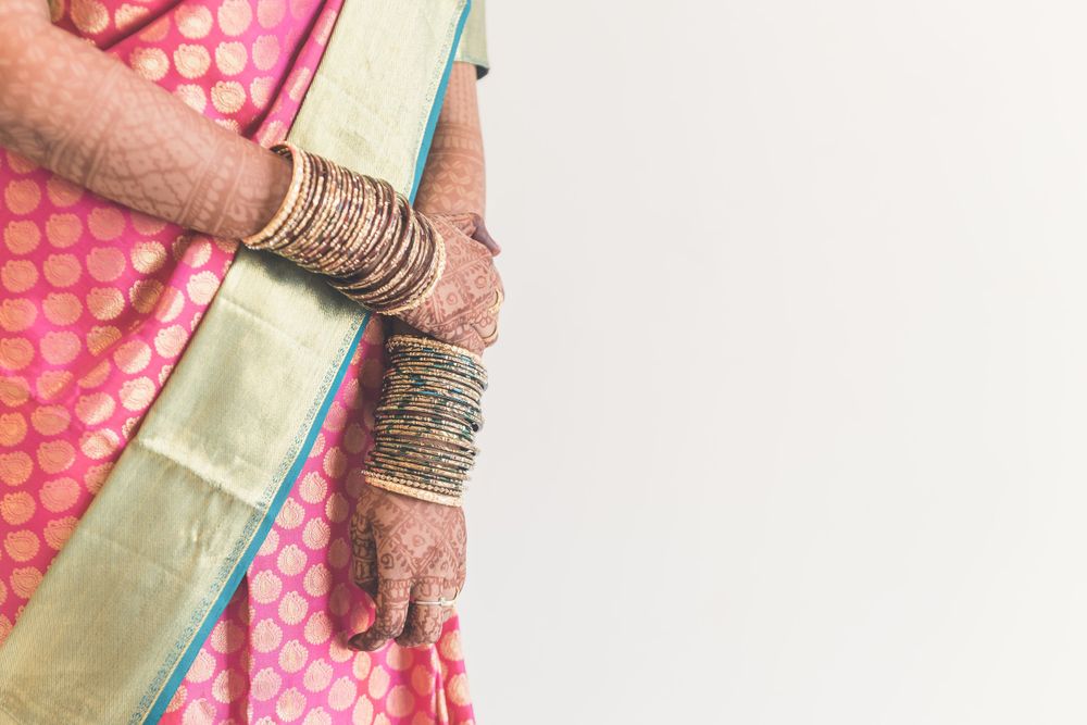 Close-up of hands adorned with mehndi designs wearing bangles and holding silk saree.
