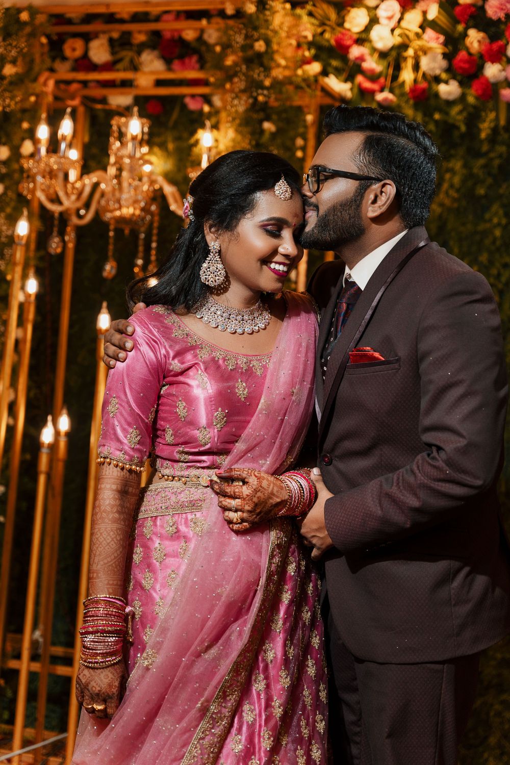 A romantic moment captured under chandeliers with floral decorations in warm lighting.