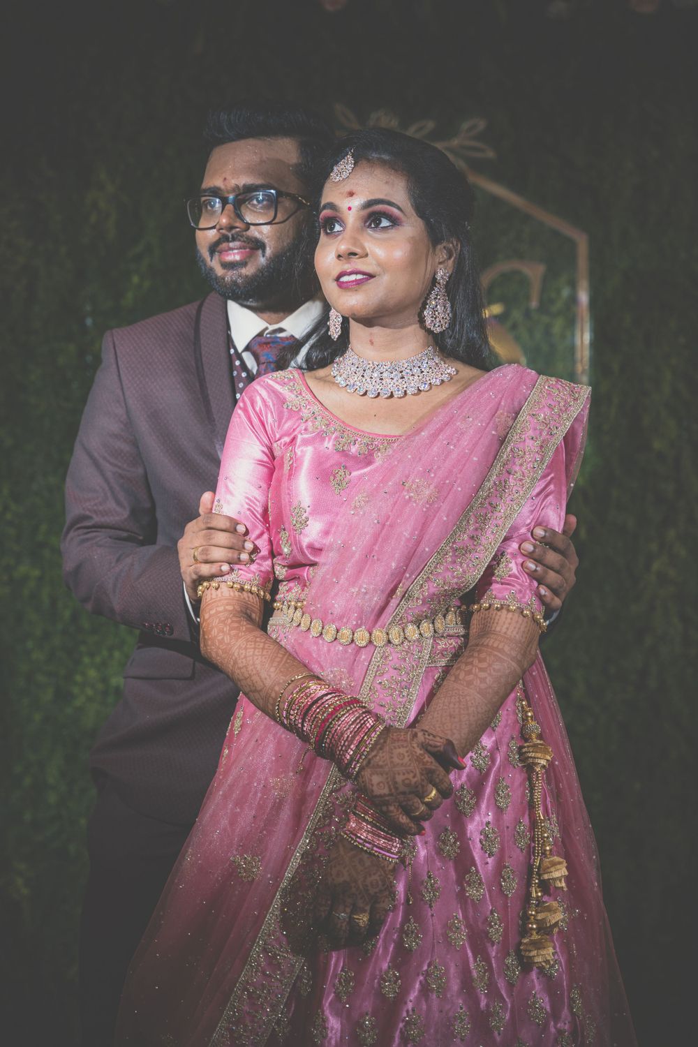 Couple in traditional Indian wedding attire posing against a dark backdrop with elegant lighting.