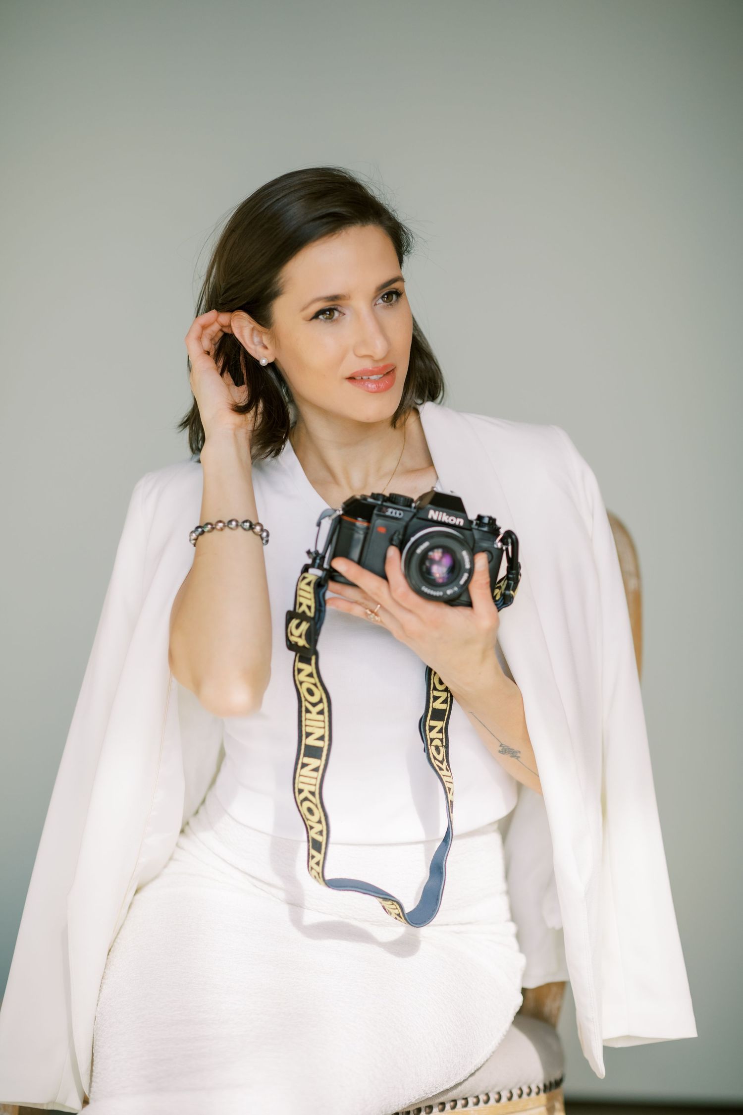 Professional photographer in white suit holding vintage camera against gray background.