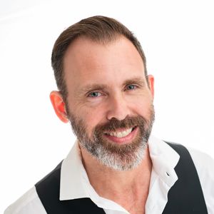 Professional headshot portrait of a smiling person wearing a white and black polo shirt.