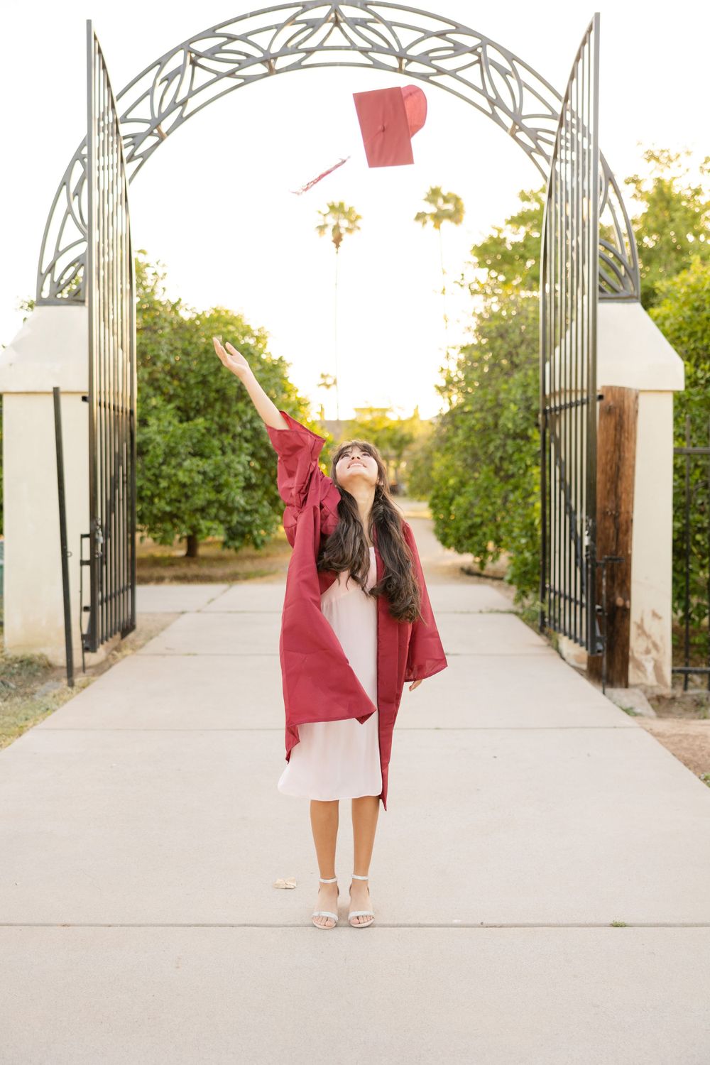 Graduate tossing cap beneath ornate metal archway entrance.