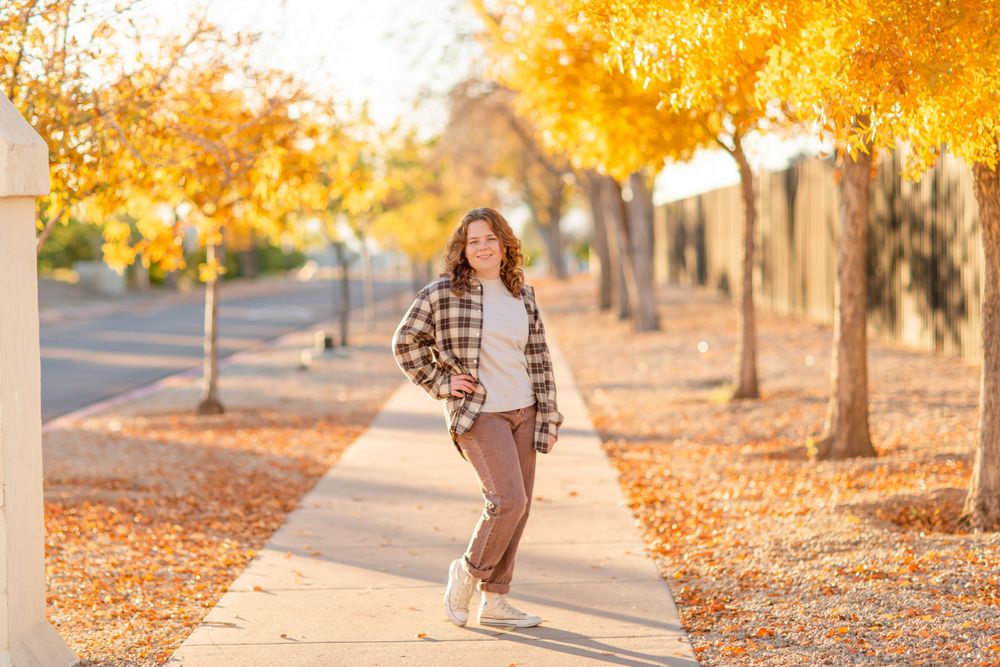 Person in casual fall outfit strolls down leaf-covered sidewalk.