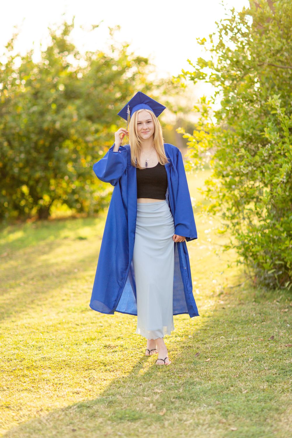 Graduate in blue cap and gown walking on grass during golden hour.