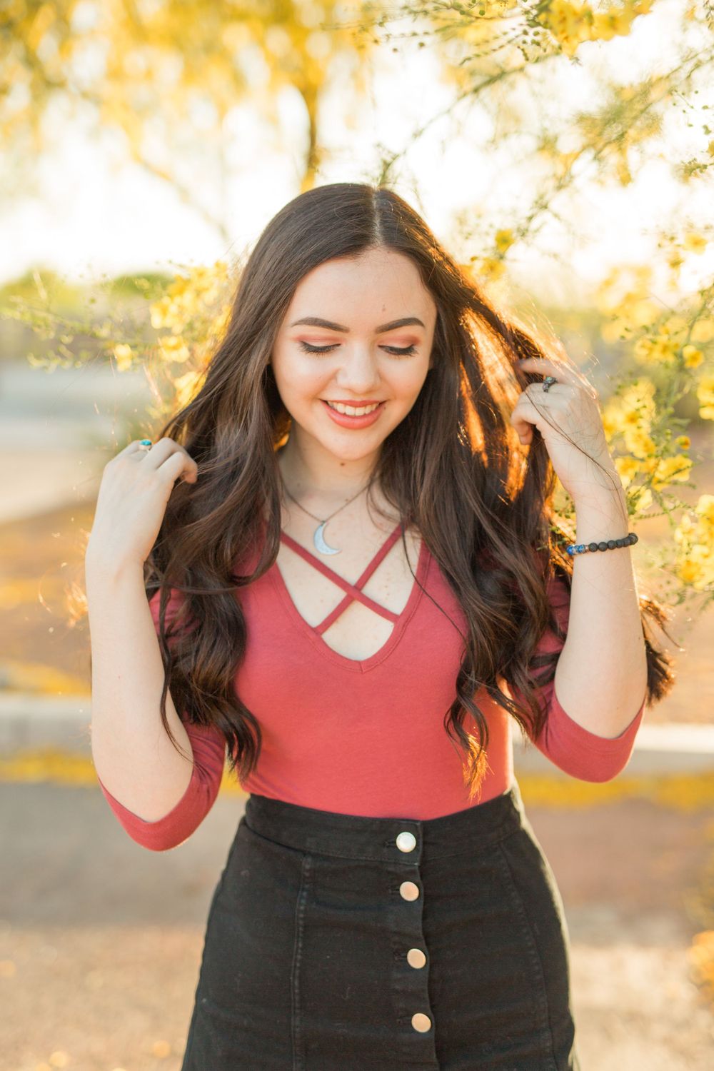 Person in red top and black skirt poses in golden sunset light.