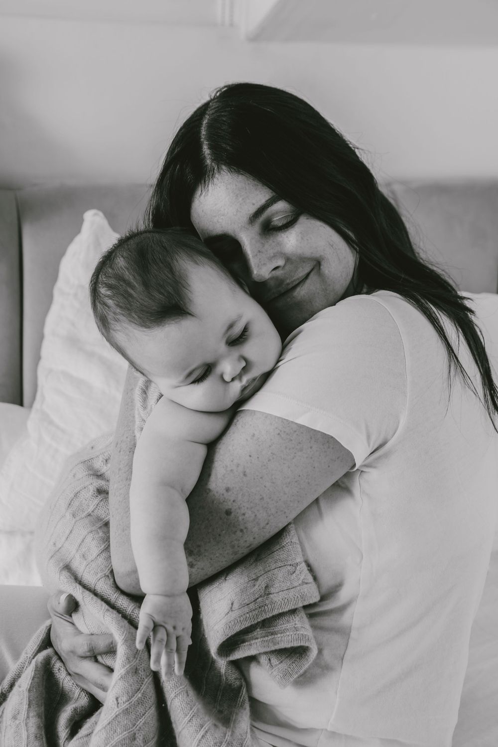 Tender black and white portrait of parent and baby cuddling with blanket on couch.