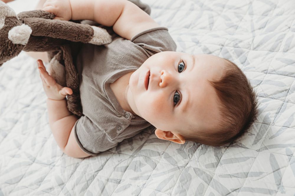 Baby relaxing on quilted blanket while holding stuffed animal toy.