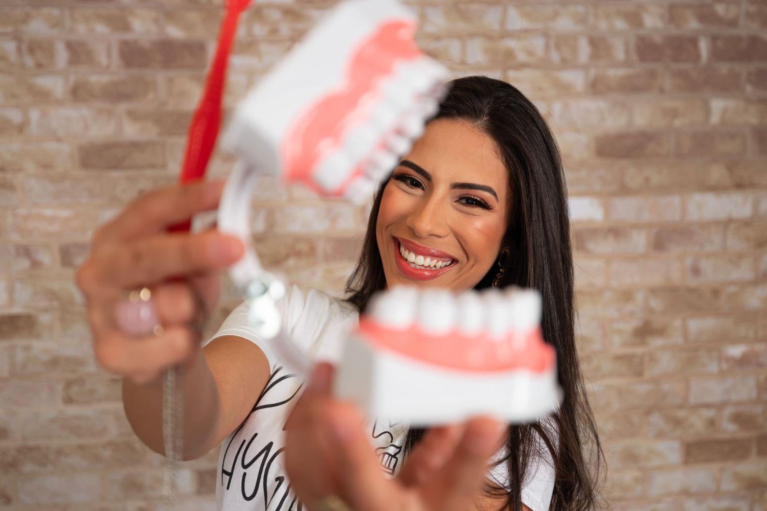 Dental professional holding up denture models against a brick wall backdrop.