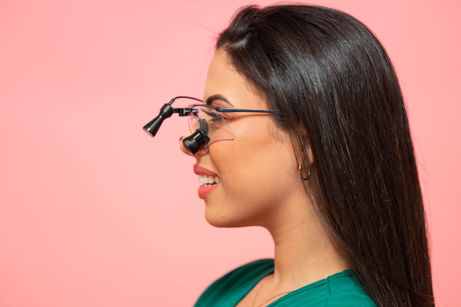 Side profile showing dental loupes worn by healthcare professional against pink background.