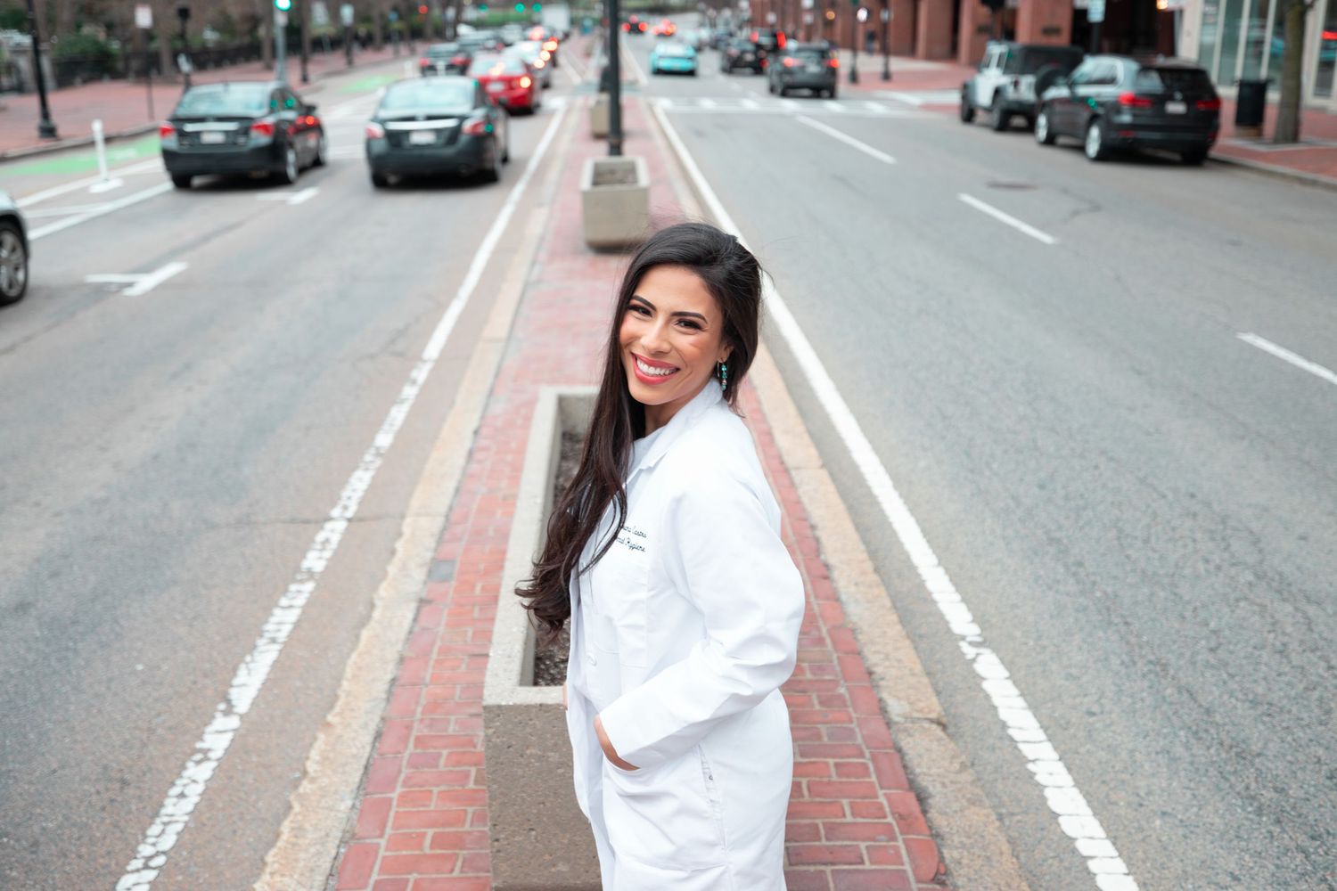 Candid street photo of someone in a white coat smiling on an urban sidewalk.