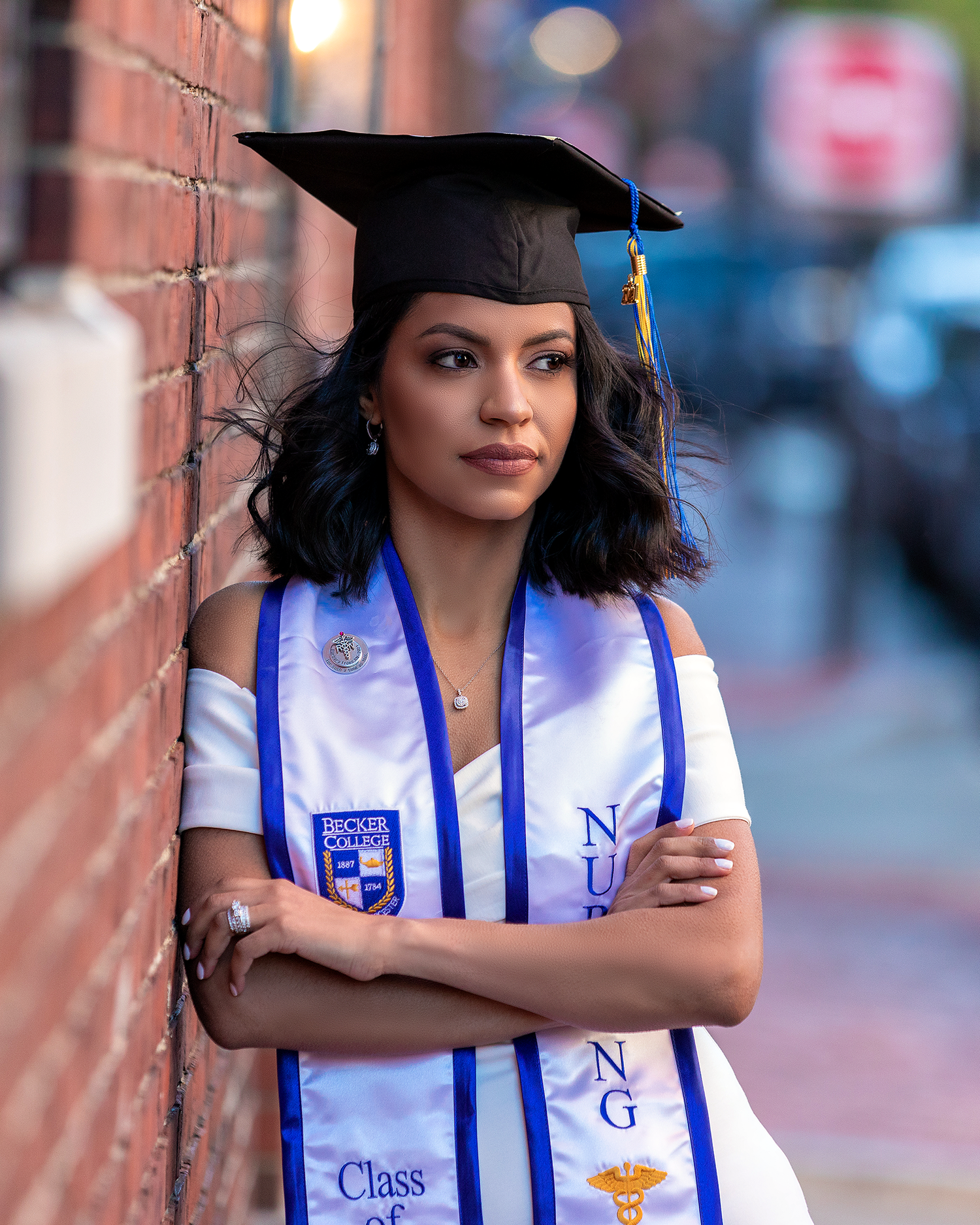 Graduate in academic regalia poses against brick wall in urban setting.