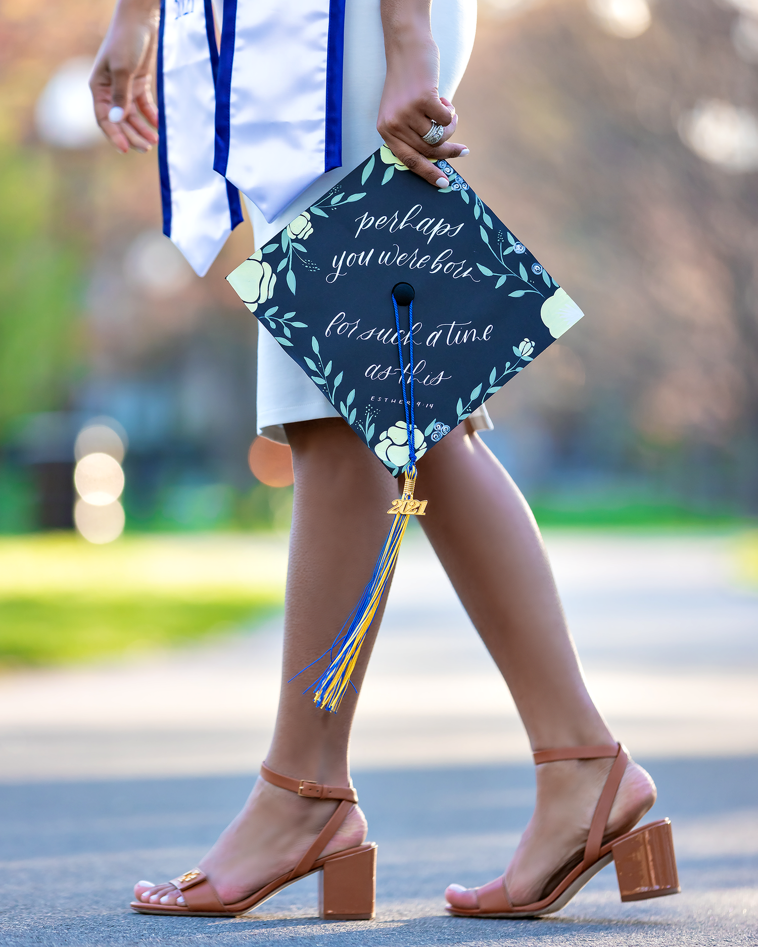 Decorated graduation cap with calligraphy and sandaled feet shown against blurred background.