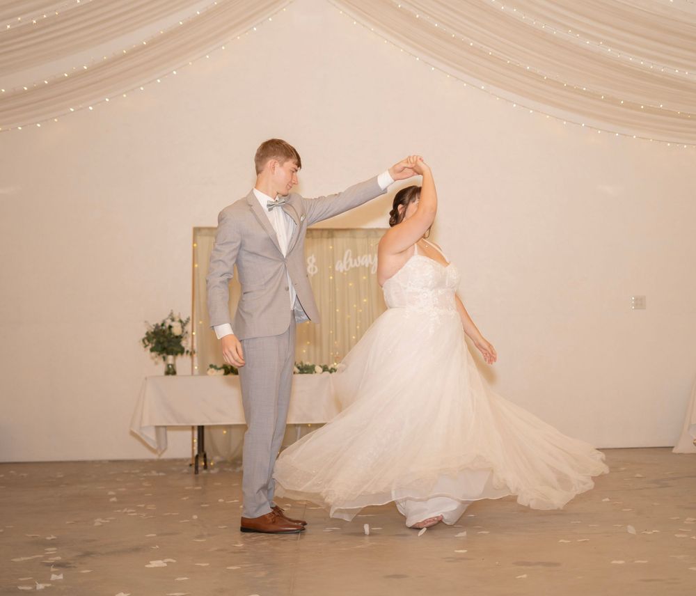 Groom twirls bride in flowing white gown during first dance at elegantly decorated wedding reception.