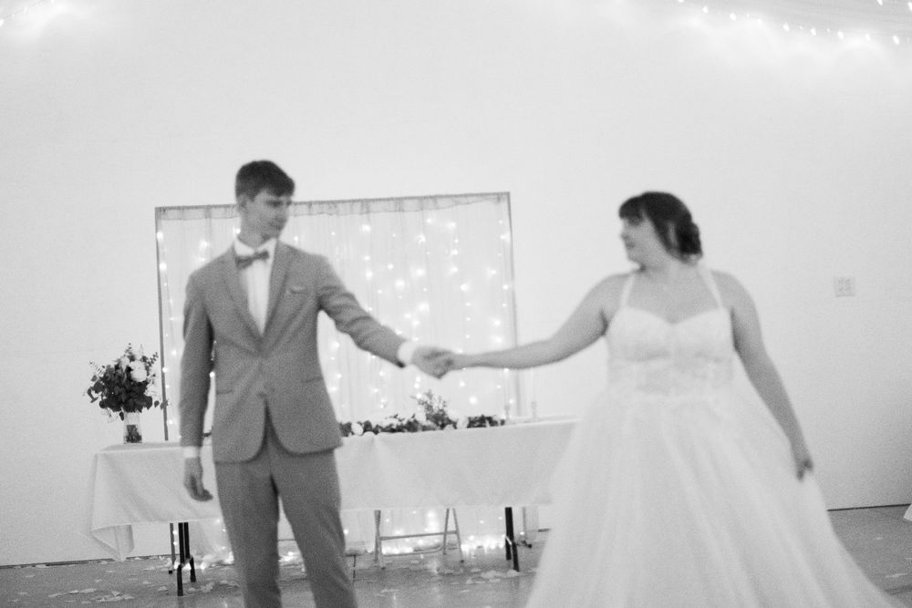 Black and white photo of bride and groom holding hands on wedding reception dance floor.