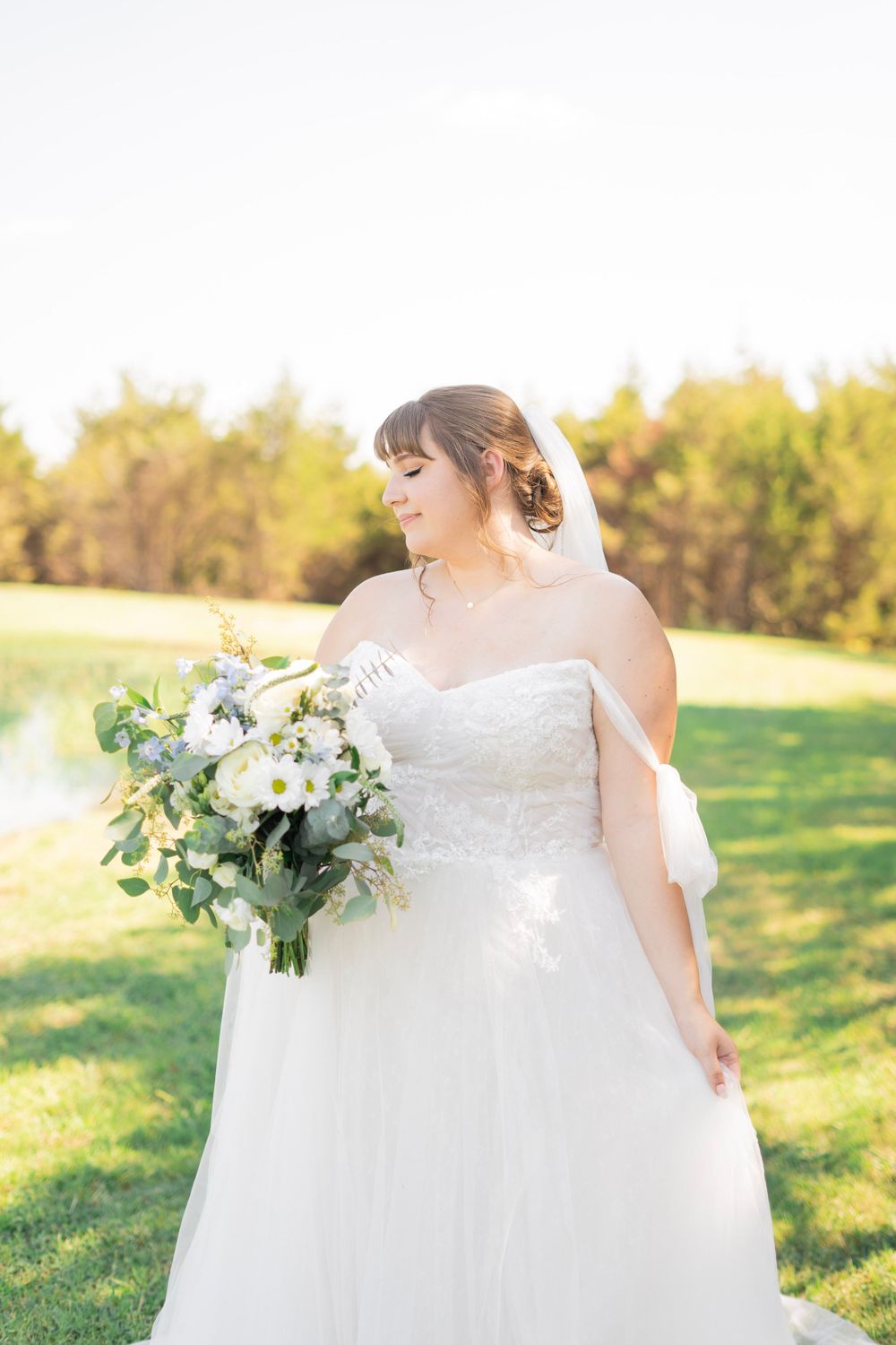 Bride in a strapless white wedding gown with veil admiring her white and green floral bouquet.