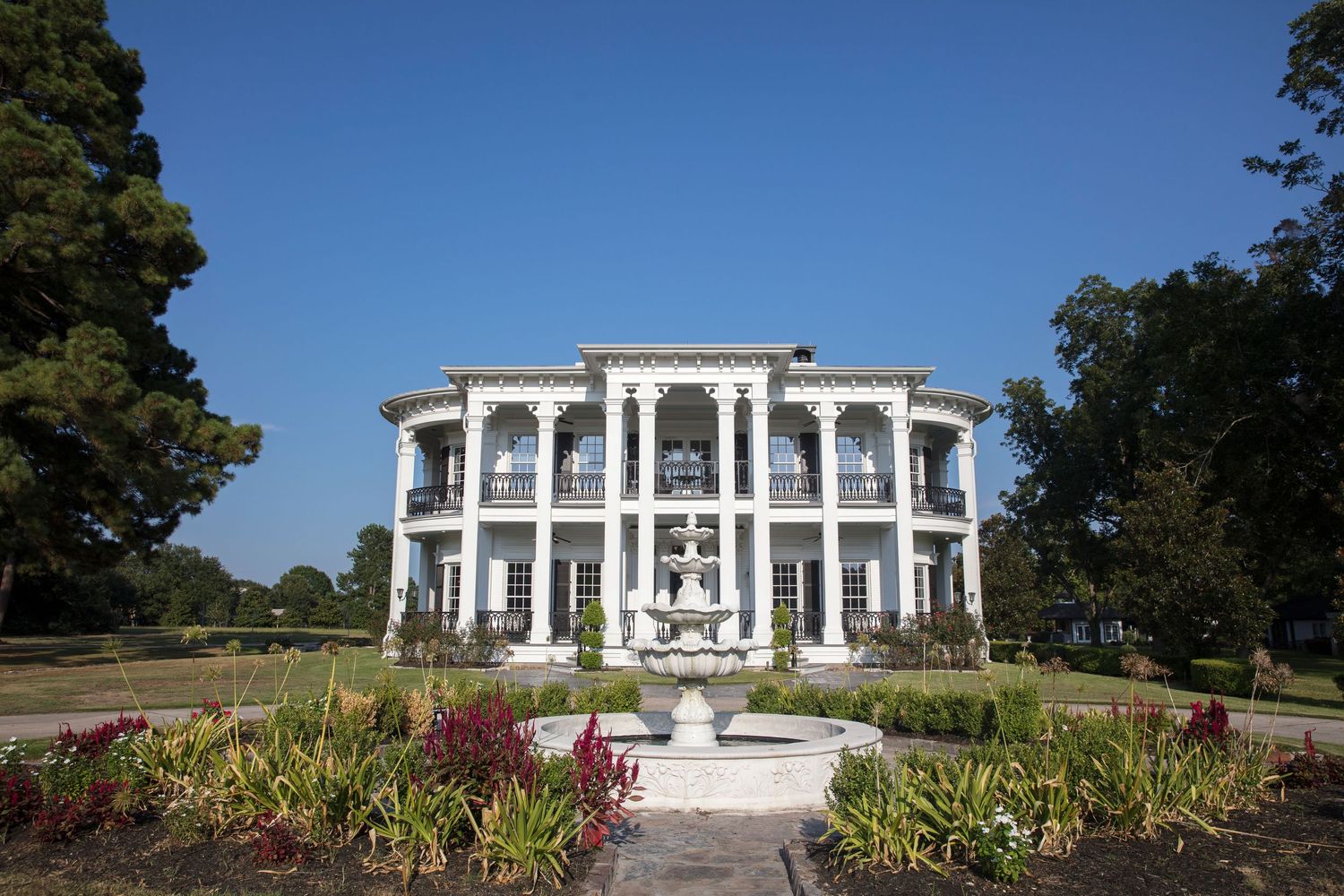 Stately white mansion with classical columns and landscaped gardens photographed under blue sky.