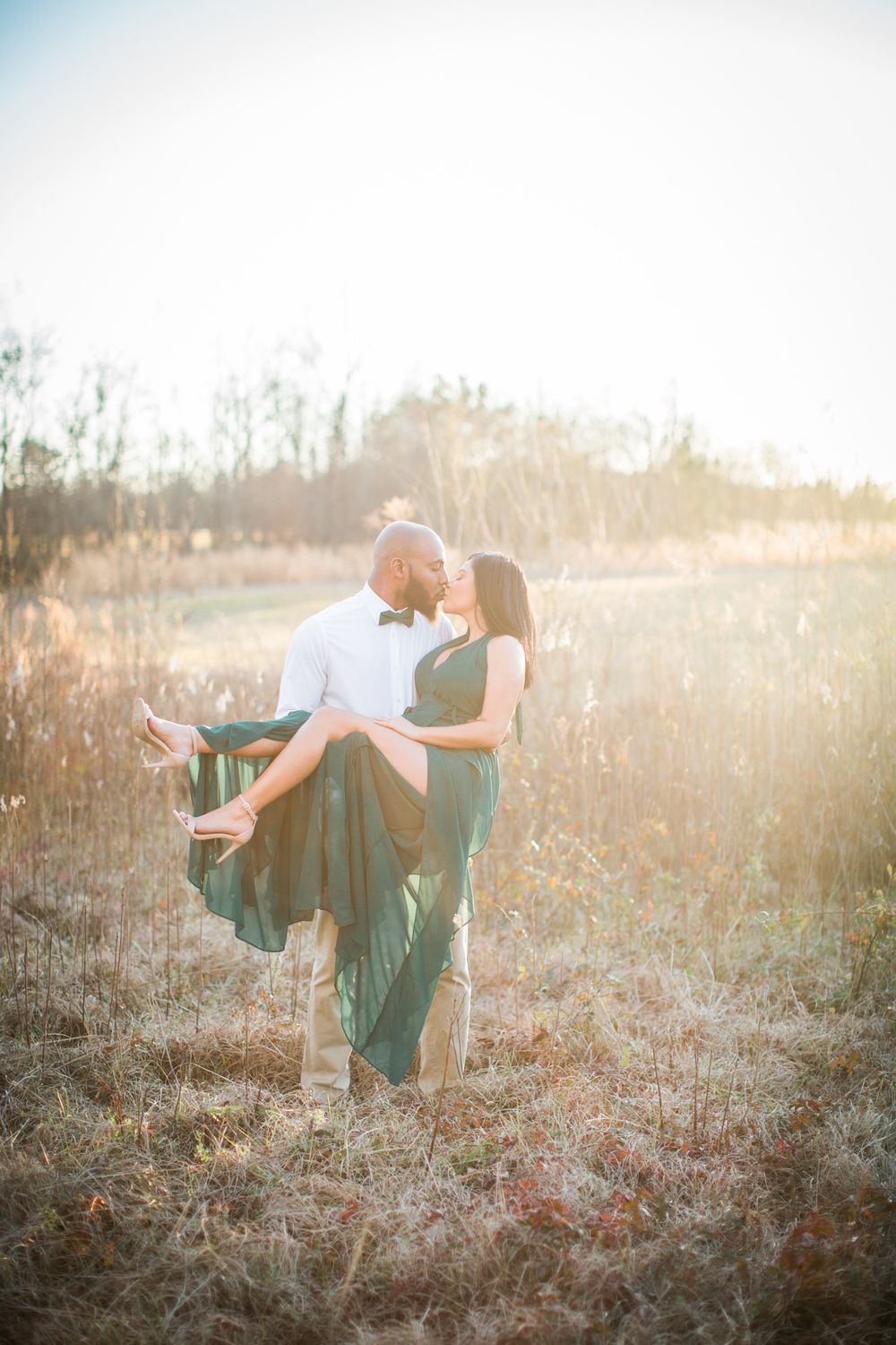 Romantic sunset engagement photo in golden field with flowing green dress.