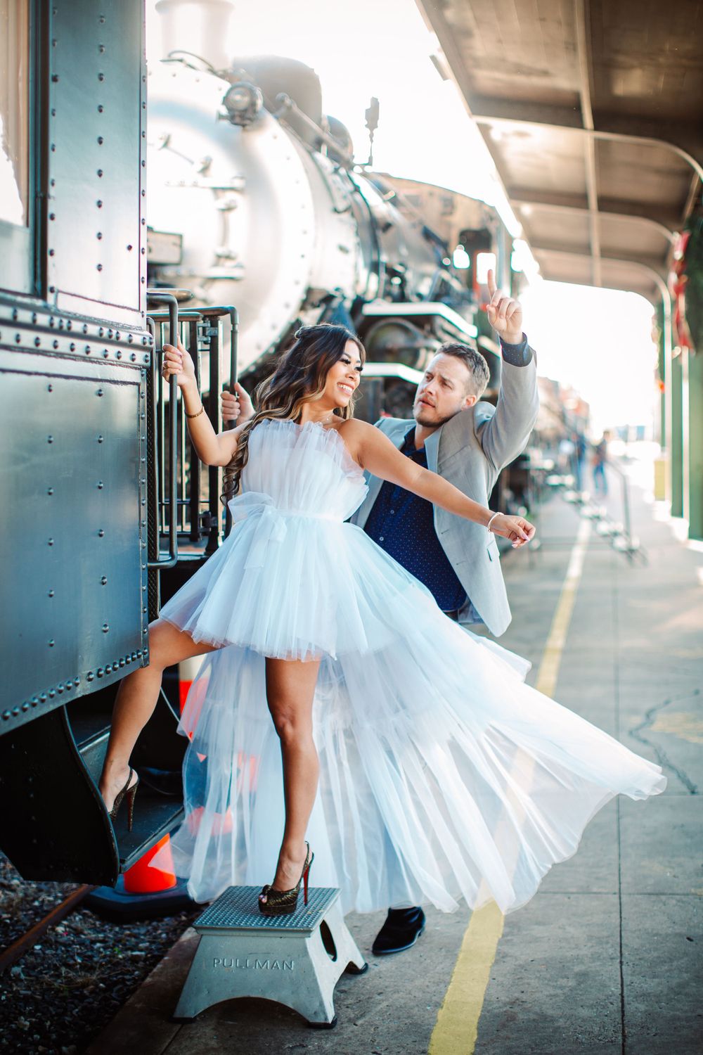 Dancing couple in formal attire pose dramatically beside vintage steam locomotive.