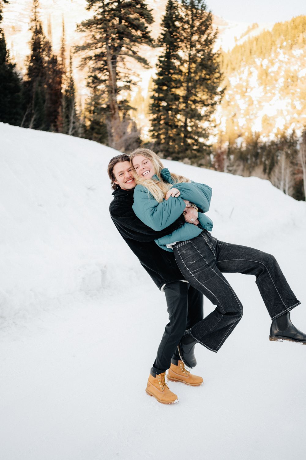 A joyful winter portrait of a couple playing in the snow with mountains in the background.