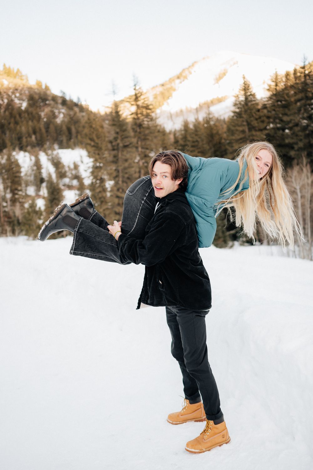 A fun winter photoshoot featuring a piggyback ride against a snowy mountain backdrop.