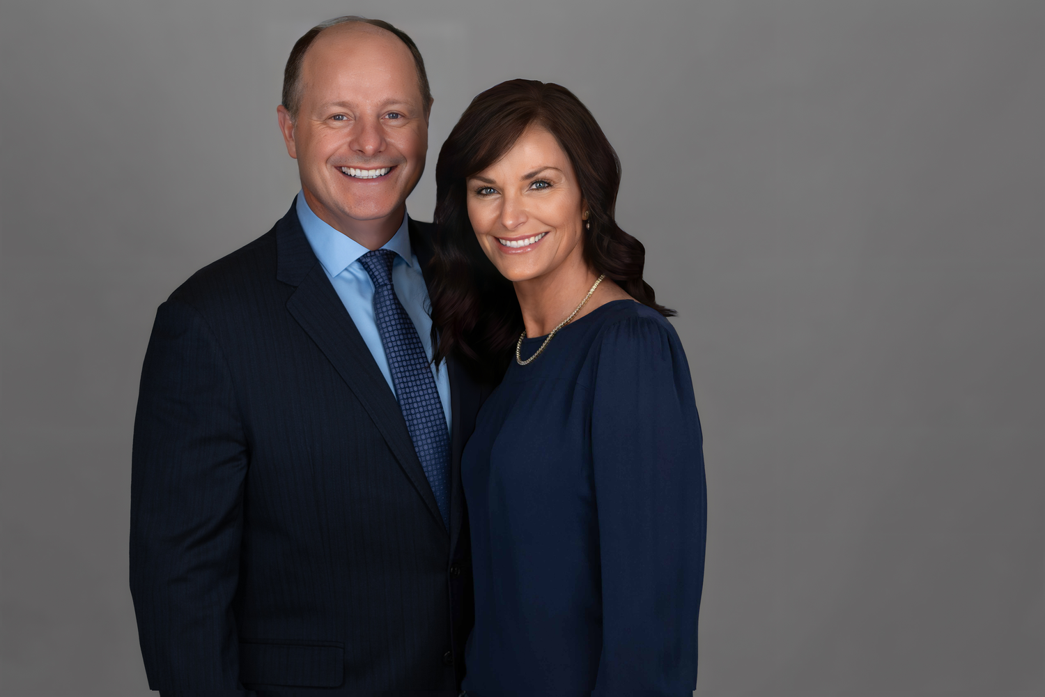 Professional headshot of couple in business attire against gray background.