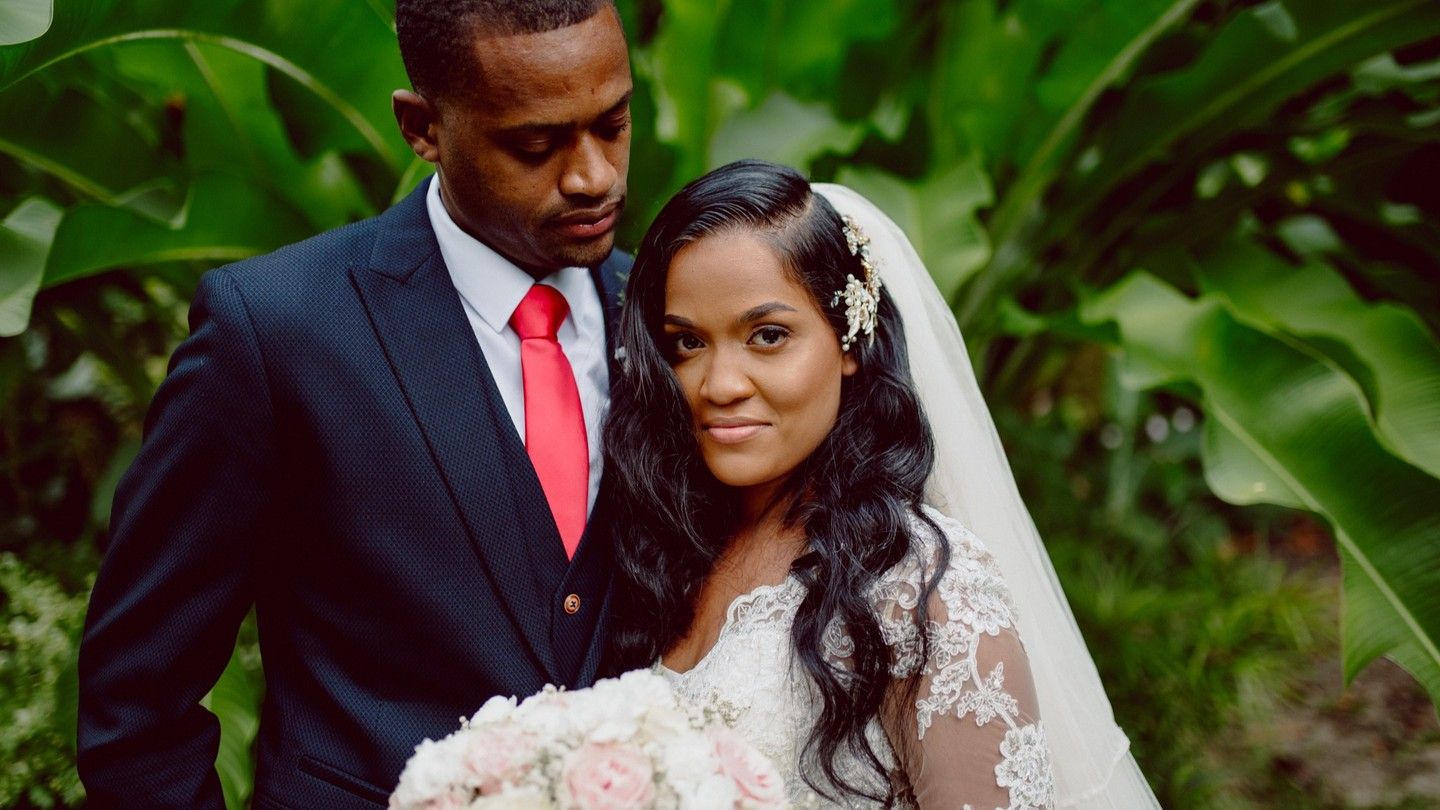 A couple poses in their wedding attire with lush greenery in the background. Waterville Estate Trinidad