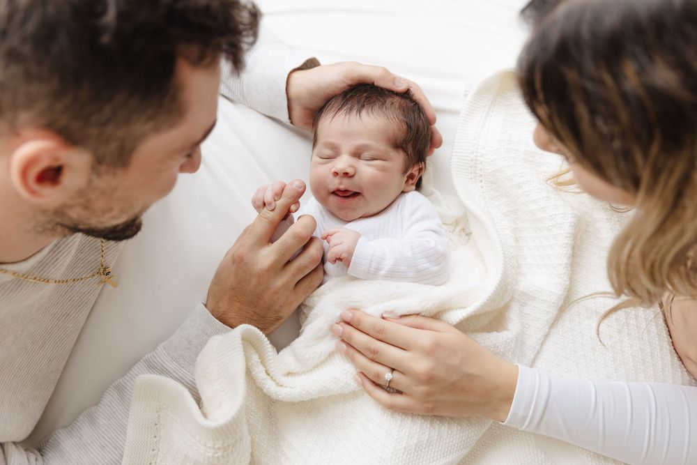 A sweet moment as parents share tender interaction with their baby laying on white bedding.