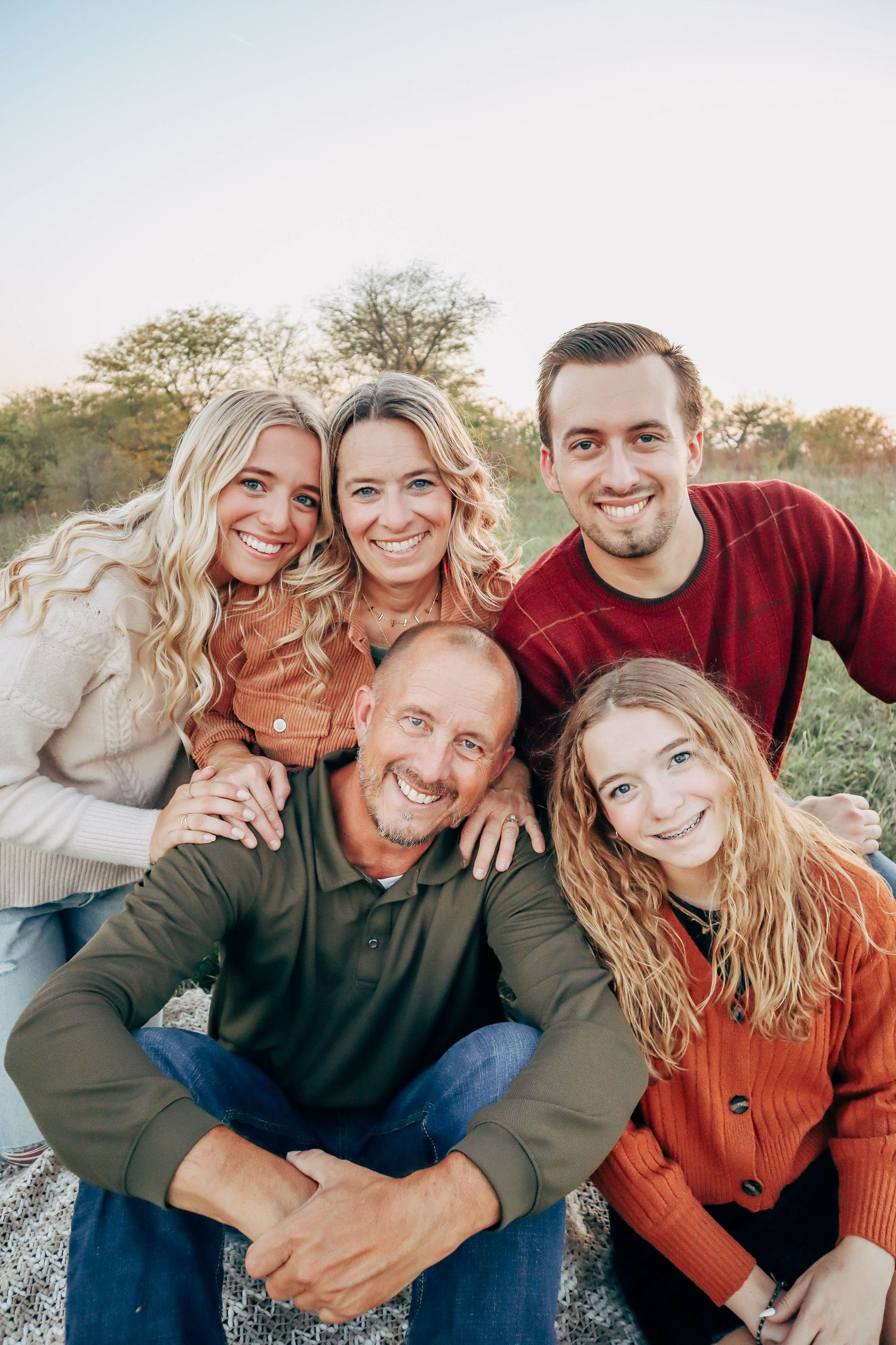 A family group photo outdoors wearing cozy fall sweaters in autumn colors.