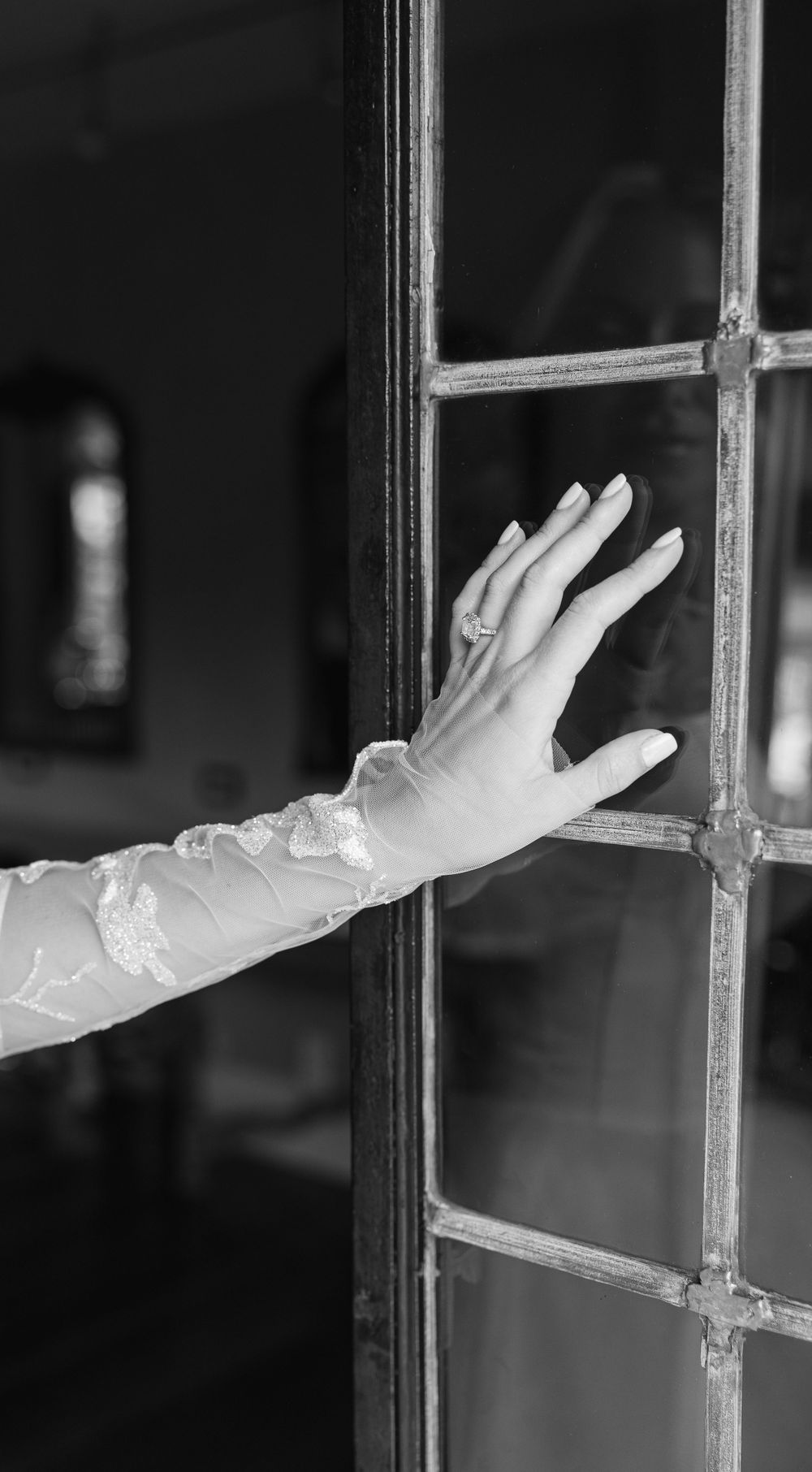 Delicate lace sleeve and engagement ring detail against window panes in black and white.