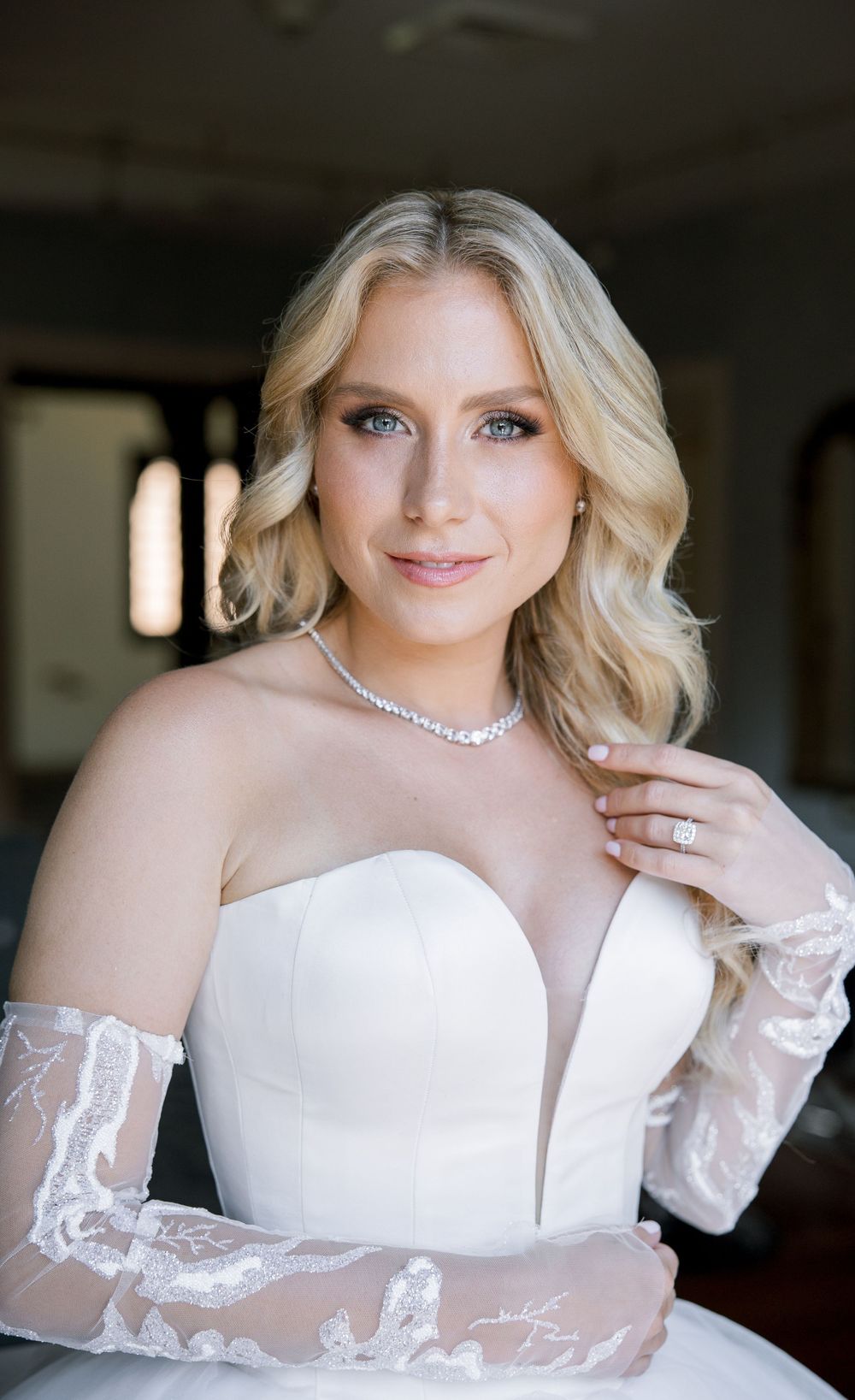 Elegant bridal portrait featuring strapless gown, lace sleeves and crystal necklace.