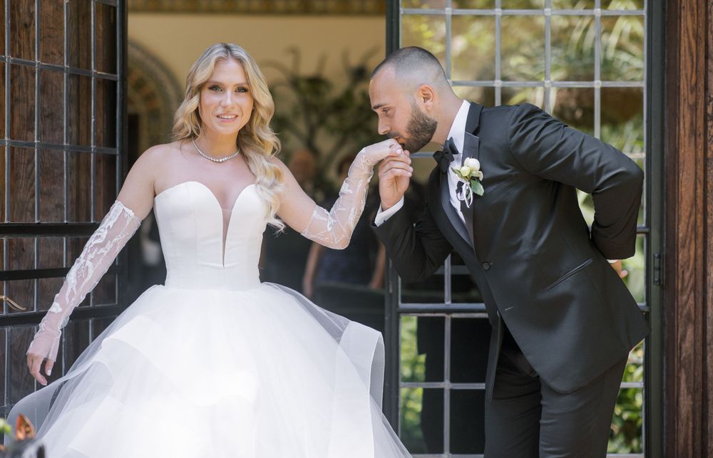 Wedding couple shares playful moment by wooden doorway in formal attire.