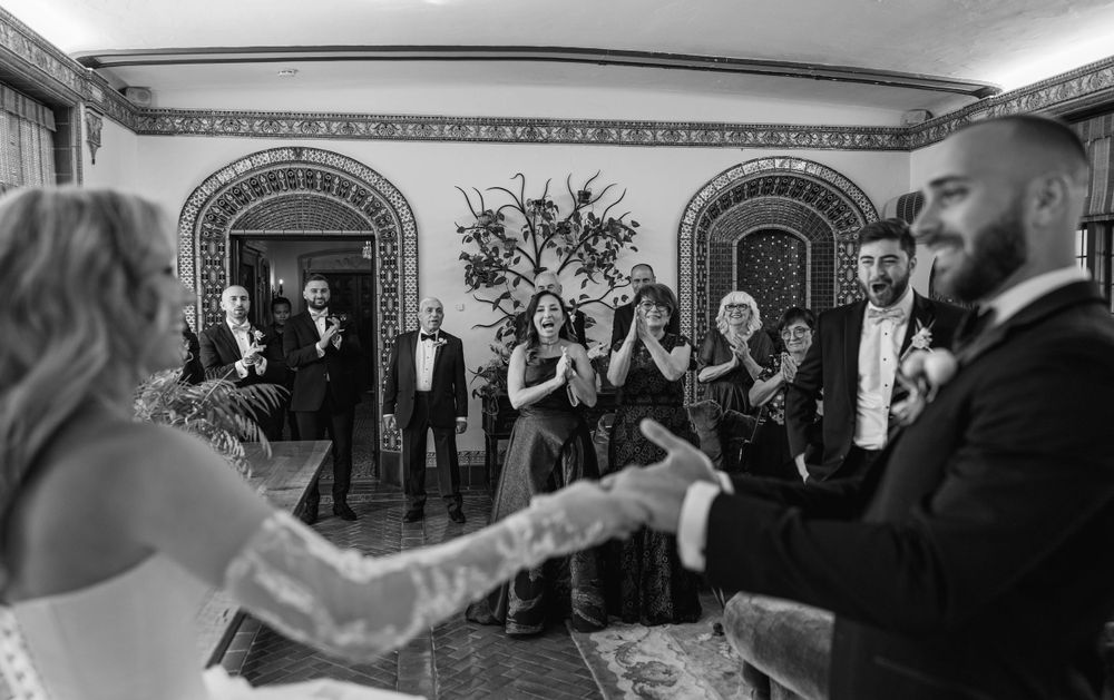 Black and white photo of wedding celebration in ornate ballroom with arched doorways.