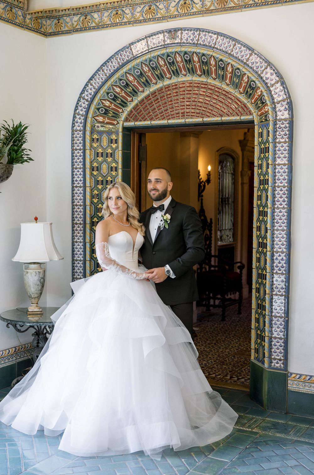 Wedding couple poses beneath ornate tiled archway in elegant venue interior.